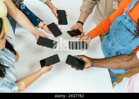 D'en haut des gens méconnaissables avec des smartphones dans les mains, formant un cercle dans un espace de travail moderne. Ce groupe diversifié, aux mains multiethniques, est Sha Banque D'Images