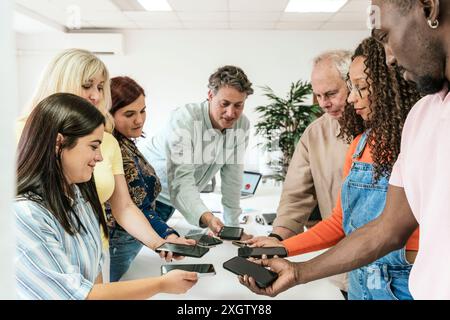 Un groupe diversifié de professionnels s’engagent dans une session collaborative dans un espace de coworking, partageant des idées et du contenu à l’aide de leurs téléphones mobiles. L'équipe Banque D'Images