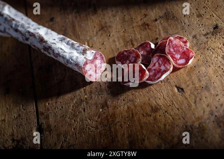 Gros plan de saucisse séchée tranchée à côté d'un fuet entier sur une surface en bois texturée, mettant en évidence les riches textures et couleurs du mea traditionnel Banque D'Images