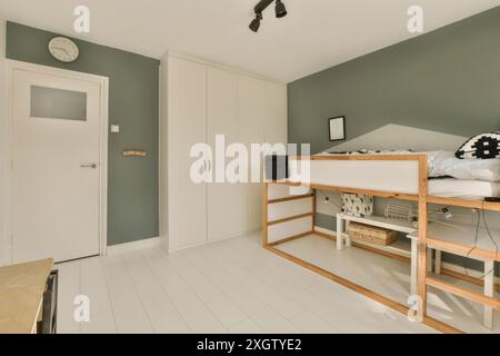 Une chambre contemporaine avec un haut lit mezzanine en bois, une élégante armoire blanche et un mur d'accent gris, mettant en valeur un design intérieur minimaliste moderne St Banque D'Images