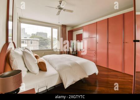 Cette chambre spacieuse et moderne dispose d''une grande armoire de couleur corail, de planchers de bois franc et d''une vue sur la ville par la fenêtre. Banque D'Images