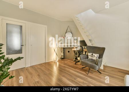 Une installation de bureau à domicile confortable avec un bureau élégant, un fauteuil confortable et un plancher en bois chaleureux, accentué par un décor de bon goût et un éclairage moderne Banque D'Images