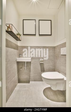 Une salle de bains moderne et élégante au design minimaliste avec des carreaux gris, des luminaires blancs et des cadres d'art mural élégants. Banque D'Images