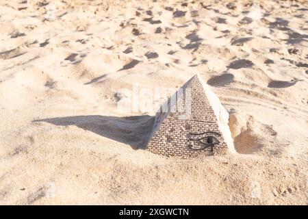 Une petite réplique en pierre d'une pyramide est cachée dans la plage de sable, créant un paysage pittoresque et symbolique Banque D'Images