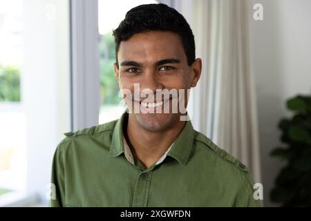 Jeune homme biracial sourit chaleureusement dans un cadre familial. Son expression joyeuse ajoute une atmosphère accueillante à l'intérieur confortable, inchangé. Banque D'Images