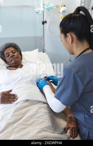 Infirmière s'occupe d'une femme afro-américaine senior dans un lit d'hôpital. Ils sont dans un cadre médical, où l'infirmière fournit des soins et du réconfort au pati Banque D'Images