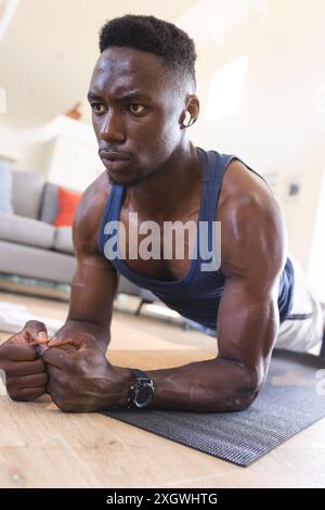 Homme afro-américain concentré exerçant à la maison, allongé sur le sol en position planche. Fitness, entraînement, exercice, vie domestique et mode de vie sain, u Banque D'Images