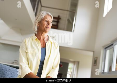 Femme caucasienne senior réfléchie assise et souriante à la maison, copiez l'espace. Bien-être, vie domestique et mode de vie des personnes âgées, inchangés. Banque D'Images