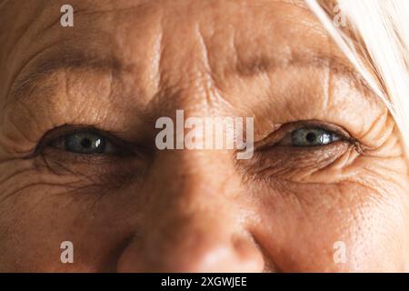 Gros plan portrait des yeux bleus d'une femme caucasienne âgée heureuse souriant à la maison. Bien-être, vie domestique et mode de vie des personnes âgées, inchangés. Banque D'Images