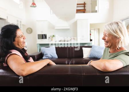 Deux amies âgées heureuses et diverses et riant assis sur le canapé dans le salon. Amitié, détente, retraite, vie domestique et vie aînée Banque D'Images