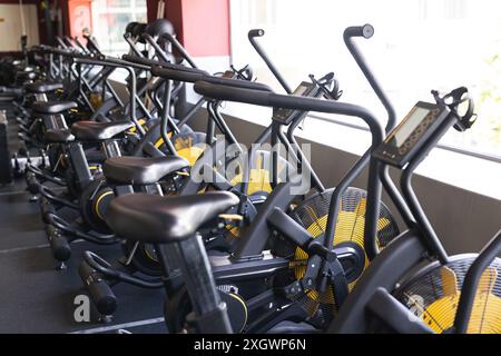 Rangée de vélos stationnaires dans un gymnase, prêt pour une séance d'entraînement. Les amateurs de fitness utilisent ces machines pour les exercices cardio et l'entraînement d'endurance. Banque D'Images