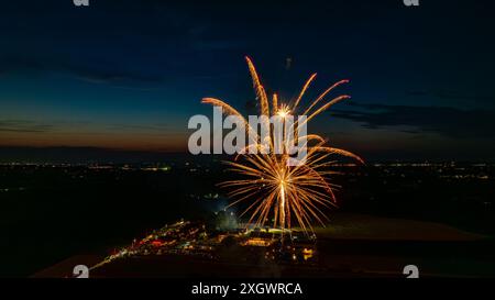 Feux d'artifice dorés explosant dans le ciel nocturne, formant des éclats radieux au-dessus des lumières lointaines de la ville et Une foule rassemblée, avec Un horizon crépusculaire ajoutant à l'atmosphère festive. Banque D'Images