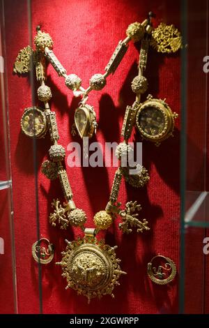 Astorga, Espagne - 4 juin 2023 : un collier orné d'or avec des motifs complexes est suspendu dans une vitrine en verre sur un fond rouge. Banque D'Images