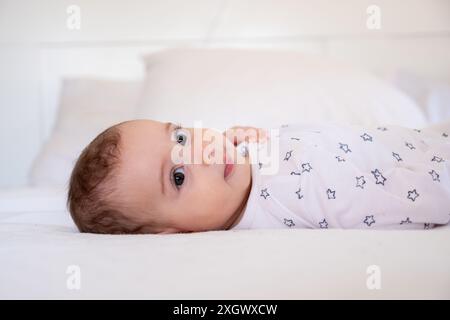 Mignon petit bébé blanc drôle s'amuser tout en étant allongé sur le lit à la maison, adorable arabian Infant Girl jouant avec ici orteils et riant tout en se reposant dedans Banque D'Images