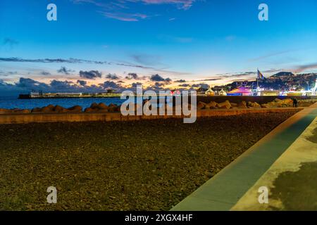 Un carnaval illuminé au coucher du soleil le long de la promenade piétonne balnéaire Praia do Almirante Reis sur la côte à la vieille ville de Funchal, îles Canaries. Banque D'Images