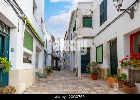Une rue étroite avec des boutiques et des cafés de trottoir dans le vieux village blanchi à la chaux historique de Mahon, en Espagne, sur l'île méditerranéenne de Minorque. Banque D'Images