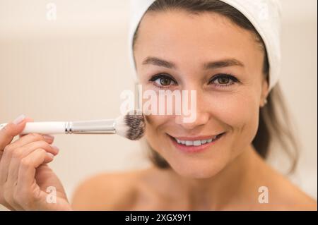 Taille vers le haut d'une femme faisant du maquillage et appliquant de la poudre sur son visage Banque D'Images