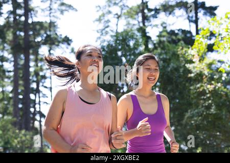Heureuses amies asiatiques portant des vêtements de sport et courant dans le parc. Activité, amitié et style de vie, inchangés. Banque D'Images