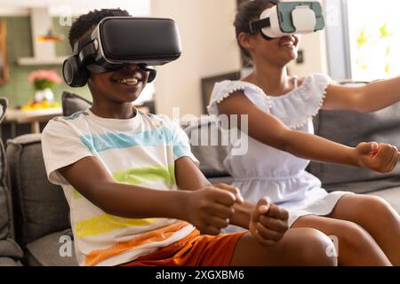 Frère biracial et sœur profiter des jeux VR à la maison. Ils sont plongés dans une expérience de réalité virtuelle, partageant un moment de joie et de divertissement. Banque D'Images