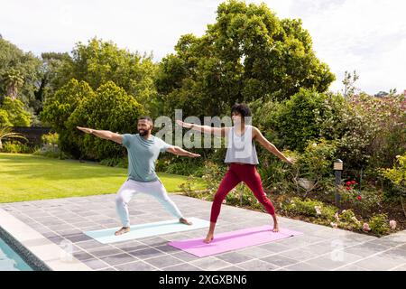 Couple biracial pratiquant le yoga en plein air, avec espace de copie. Ils profitent d'un style de vie sain dans un jardin serein. Banque D'Images