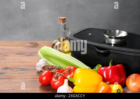 Pot noir avec couvercle en verre, épices et légumes sur table en bois Banque D'Images