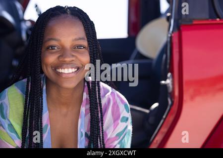 Une jeune femme afro-américaine sourit avec éclat lors d’un Road trip, avec un espace de copie. Son expression joyeuse ajoute de la chaleur au cadre extérieur. Banque D'Images
