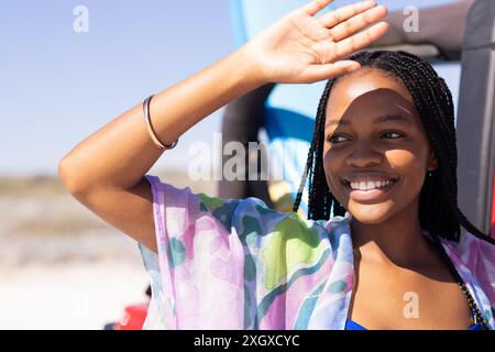 La jeune femme afro-américaine protège ses yeux du soleil lors d'un voyage en voiture. Le cadre extérieur la capture en profitant d'une journée lumineuse et ensoleillée. Banque D'Images