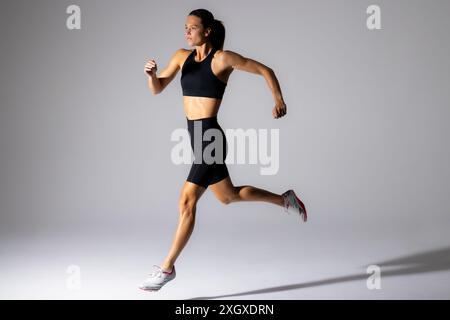 Jeune athlète féminine caucasienne sprints dans un cadre de studio, avec un espace de copie sur fond blanc. Une tenue sportive met en valeur sa vie axée sur la forme physique Banque D'Images
