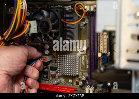 Main d'un technicien débranchant l'alimentation de la carte mère d'un ordinateur. Banque D'Images