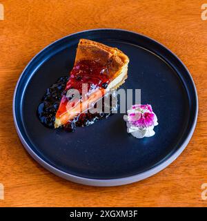Une délicieuse tranche de cheesecake avec garniture de sauce aux baies servie sur une assiette noire Banque D'Images