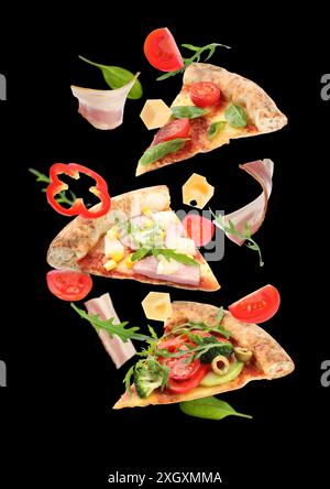 Tranches de pizza savoureuse et ingrédients dans l'air sur fond noir Banque D'Images