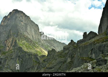 Une crête rocheuse pointue d'une haute falaise aux pentes abruptes relie deux hautes montagnes pour former un col sous un ciel nuageux d'été. Parc naturel d'Ergaki, Kra Banque D'Images