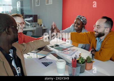 Groupe de collègues divers au bureau pendant la réunion. Des professionnels souriants démontrant le travail d'équipe et l'unité autour de la table avec des documents et des appareils numériques Banque D'Images