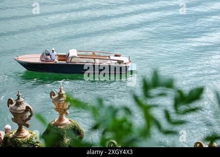 Un hors-bord classique en bois attend avec son chauffeur sur le lac turquoise en contrebas de Villa del Balbianello sur le lac de Côme, en Italie. Banque D'Images