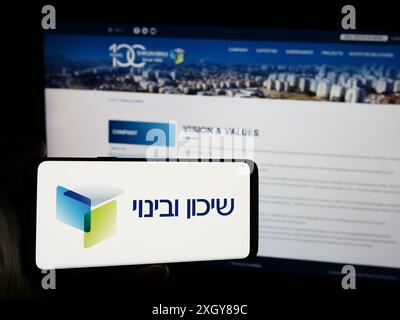 Personne tenant un smartphone avec le logo de la société de développement israélienne Shikun et Binui en face du site Web. Concentrez-vous sur l'affichage du téléphone. Banque D'Images