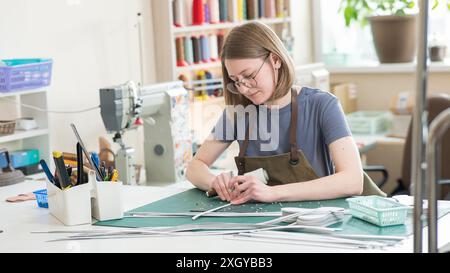 Une femme fait des trous dans une ceinture en cuir dans un atelier. Banque D'Images