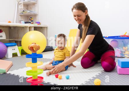 Physiothérapeute aidant un jeune enfant atteint de troubles neurodéveloppementaux tout en physiothérapie pour la motricité et la correction de la coordination défectueuse Banque D'Images