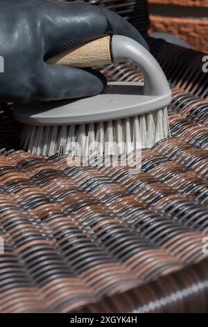 Personne frottant une chaise de jardin en rotin avec une brosse à main. Concept de corvée de travail ménager à la maison de jardin. Banque D'Images