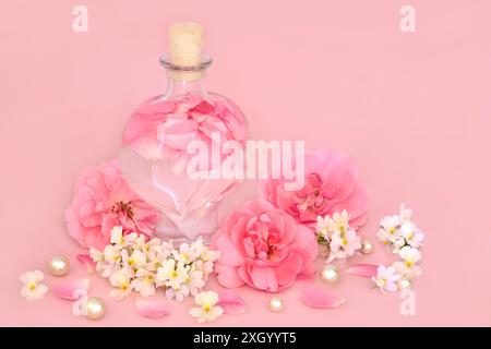 Parfum de fleur de rose et de nemesia en bouteille en forme de coeur sur rose avec des fleurs et des perles en vrac. Produit de beauté, cadeau pour la Saint-Valentin, anniversaire. Banque D'Images