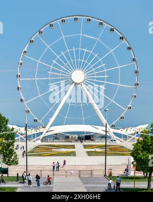 Bakou, Azerbaïdjan - 4 mai 2024 : vue de la grande roue Baku Eye, située à côté du centre commercial Deniz. La roue est en arrière-plan avec des gens marchant au premier plan. Banque D'Images
