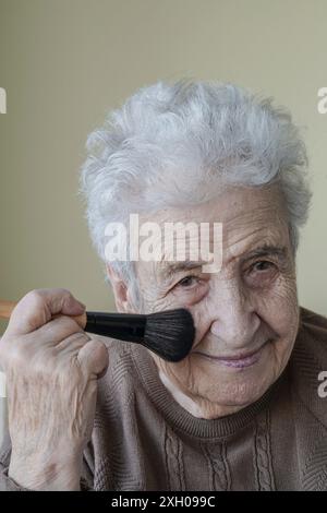 Une belle femme âgée se maquillant avec un pinceau. portrait des personnes âgées. Banque D'Images