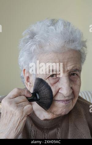 Une belle femme âgée se maquillant avec un pinceau. portrait des personnes âgées. Banque D'Images