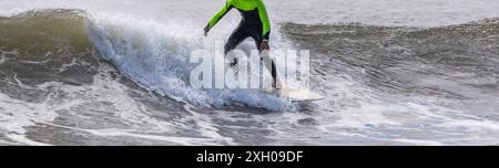 Vue horizontale d'un garçon surfant sur une vague brisée portant une combinaison noire et vert fluo à Giglo Beach long Island. Banque D'Images