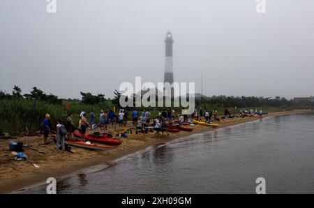 Fire Island, New York, États-Unis - 9 juillet 2024 : un groupe de personnes est rassemblé sur un rivage sablonneux, préparant des kayaks près du phare de Fire Island sur un fo Banque D'Images