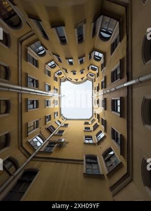 Plan vertical regardant dans une cour urbaine avec des murs jaunes et plusieurs fenêtres. Capturer la symétrie architecturale. Banque D'Images