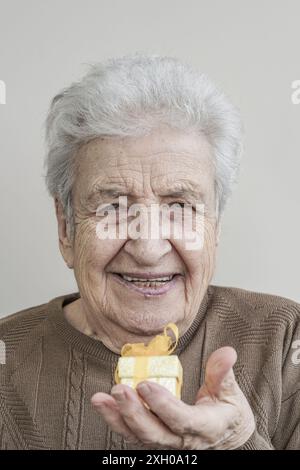 Une femme âgée tenant une petite boîte cadeau Banque D'Images