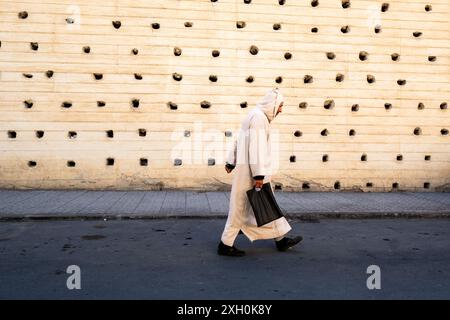 Composition d'un homme marchant dans la rue vêtu d'une djellaba Bourgogne devant l'immense mur de la ville de Fès au Maroc, en Afrique du Nord Banque D'Images