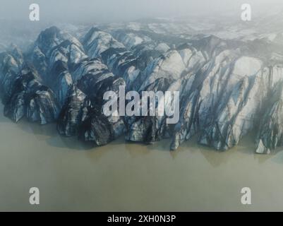 Vue aérienne des formations glaciaires spectaculaires du glacier Sólheimajokull en Islande, mettant en valeur les motifs et textures saisissants de la glace glaciaire. Banque D'Images