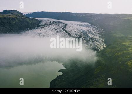 Une vue aérienne panoramique du glacier Sólheimajokull en Islande, avec des montagnes verdoyantes, un lagon glaciaire et une couche de brume. Banque D'Images
