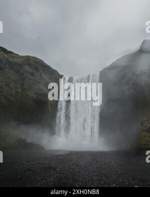 Vue rapprochée de la puissante cascade de Skogafoss en Islande, entourée de brume et de falaises spectaculaires. Banque D'Images